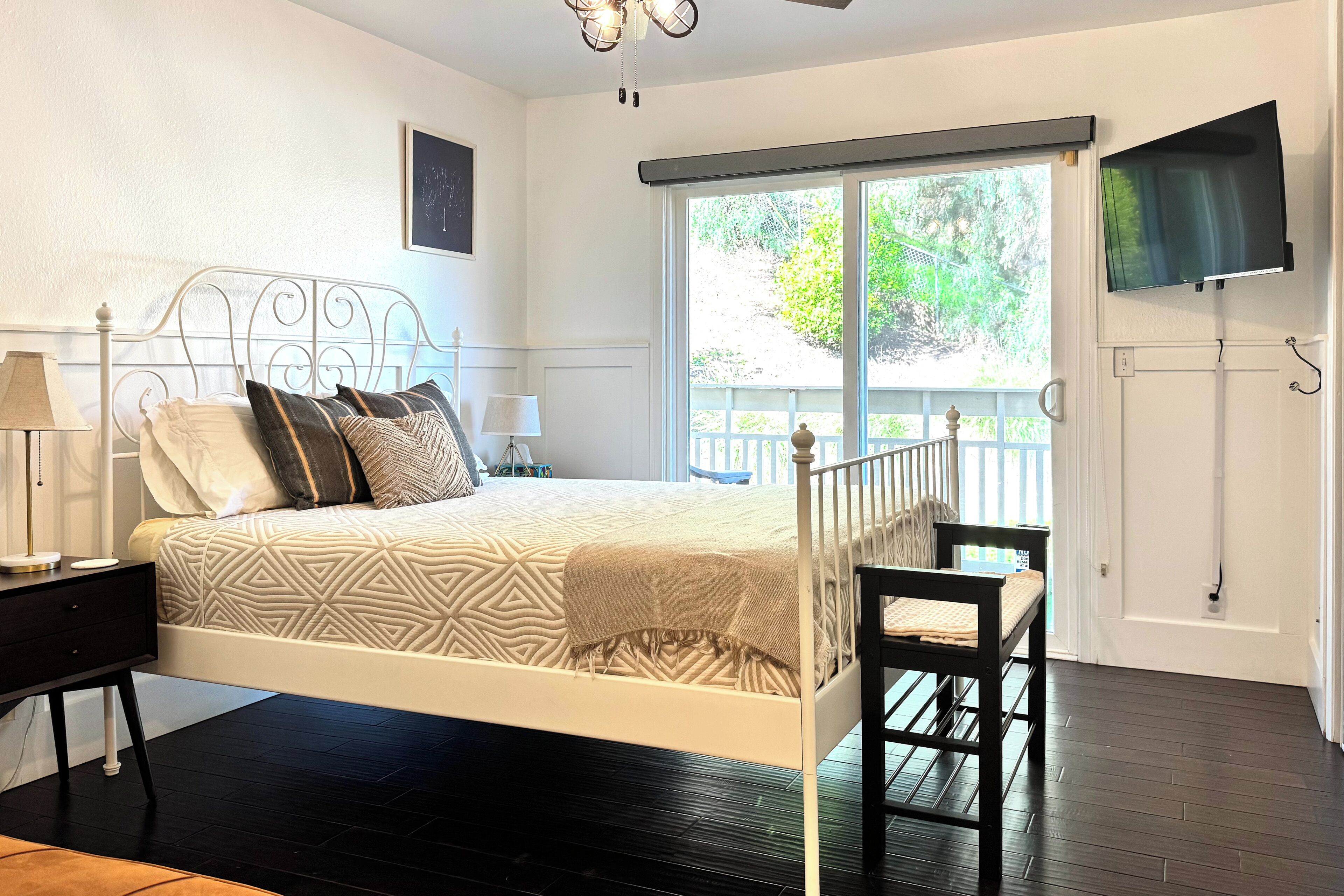 A bedroom with a bed, nightstands, a chair, a TV, and a large window.