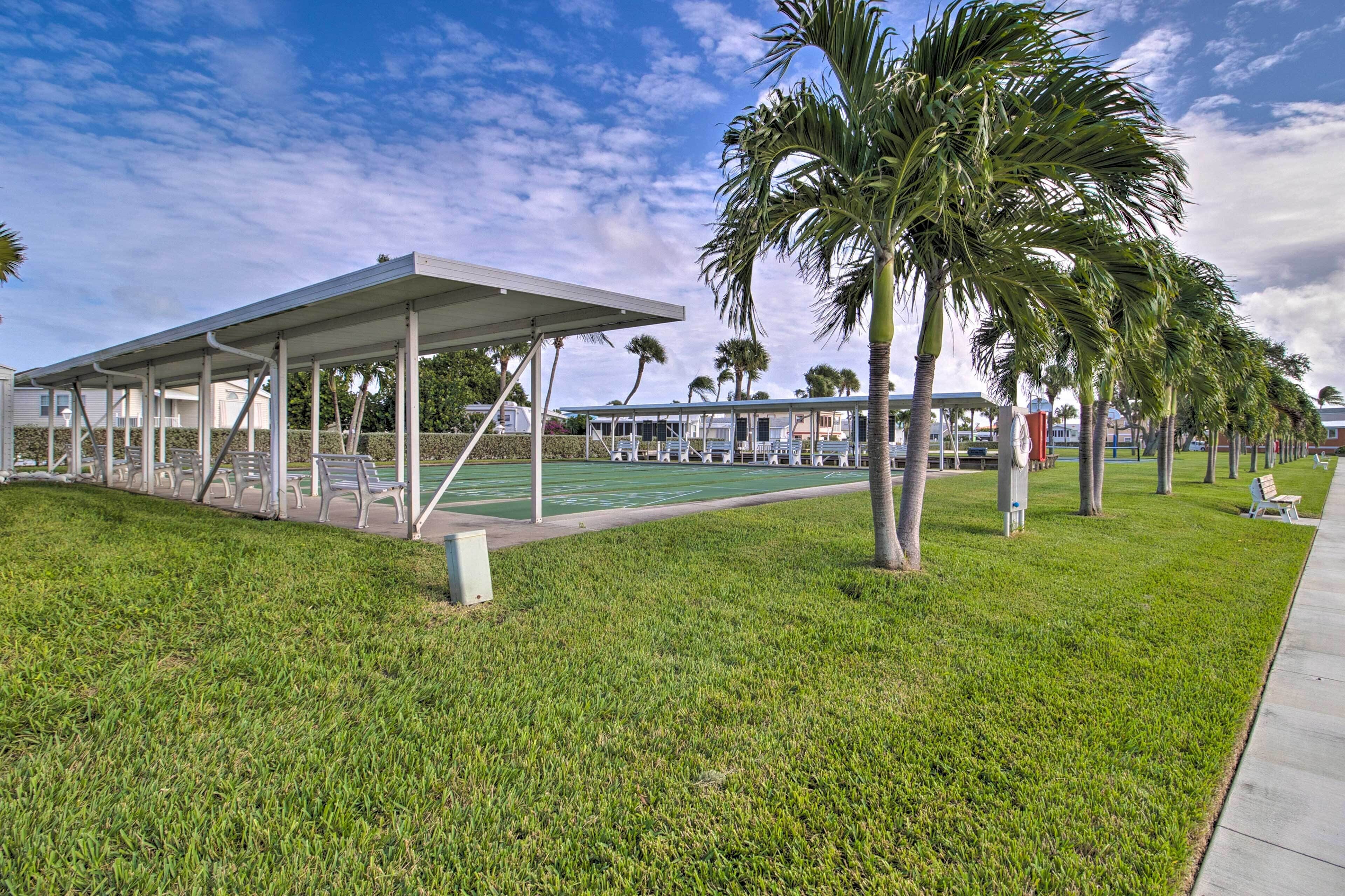 A covered outdoor area with a green lawn, palm trees, and a row of white chairs.