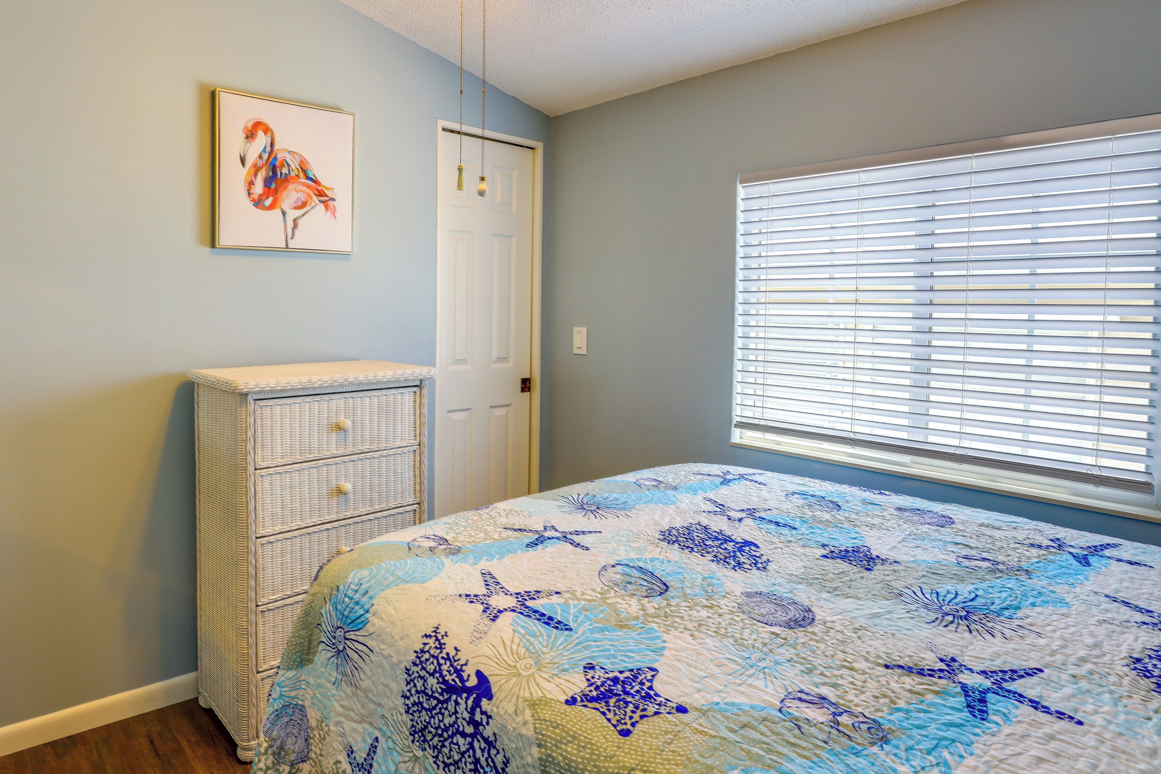 A bedroom with a bed, a dresser, a door, and a window with blinds.
