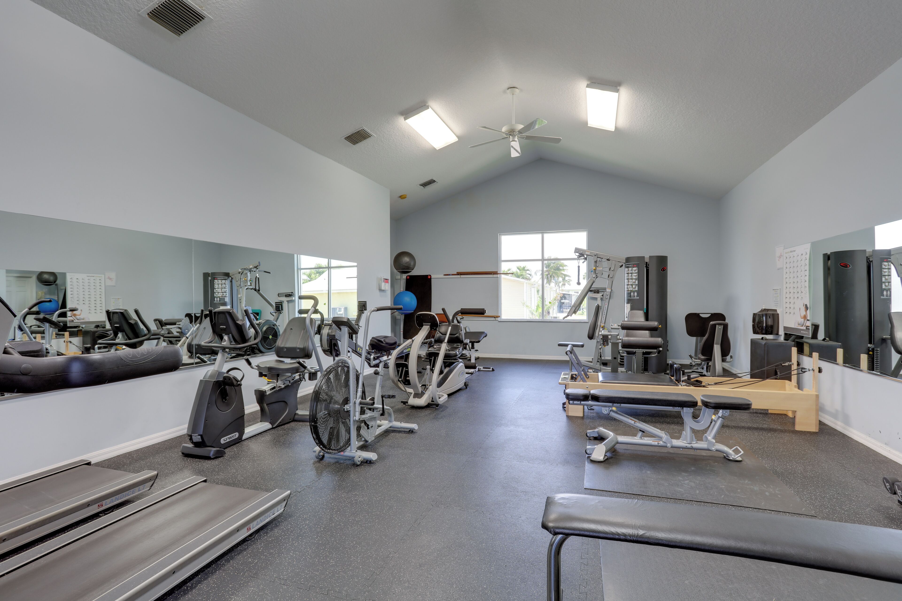 A gym with various exercise equipment, a ceiling fan, and large windows.