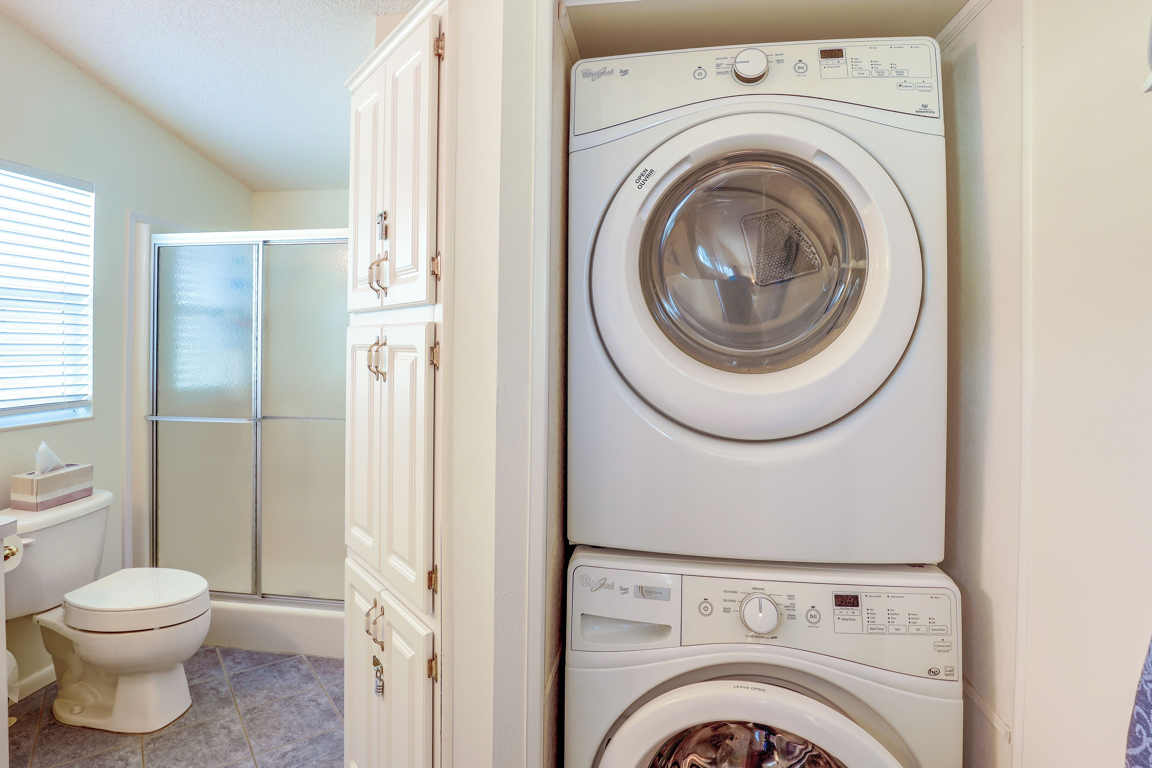 A compact laundry room with a front-loading washer and dryer, a toilet, and a shower area.