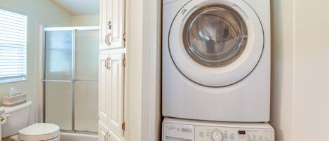 A compact laundry room with a front-loading washer and dryer, a toilet, and a shower area.