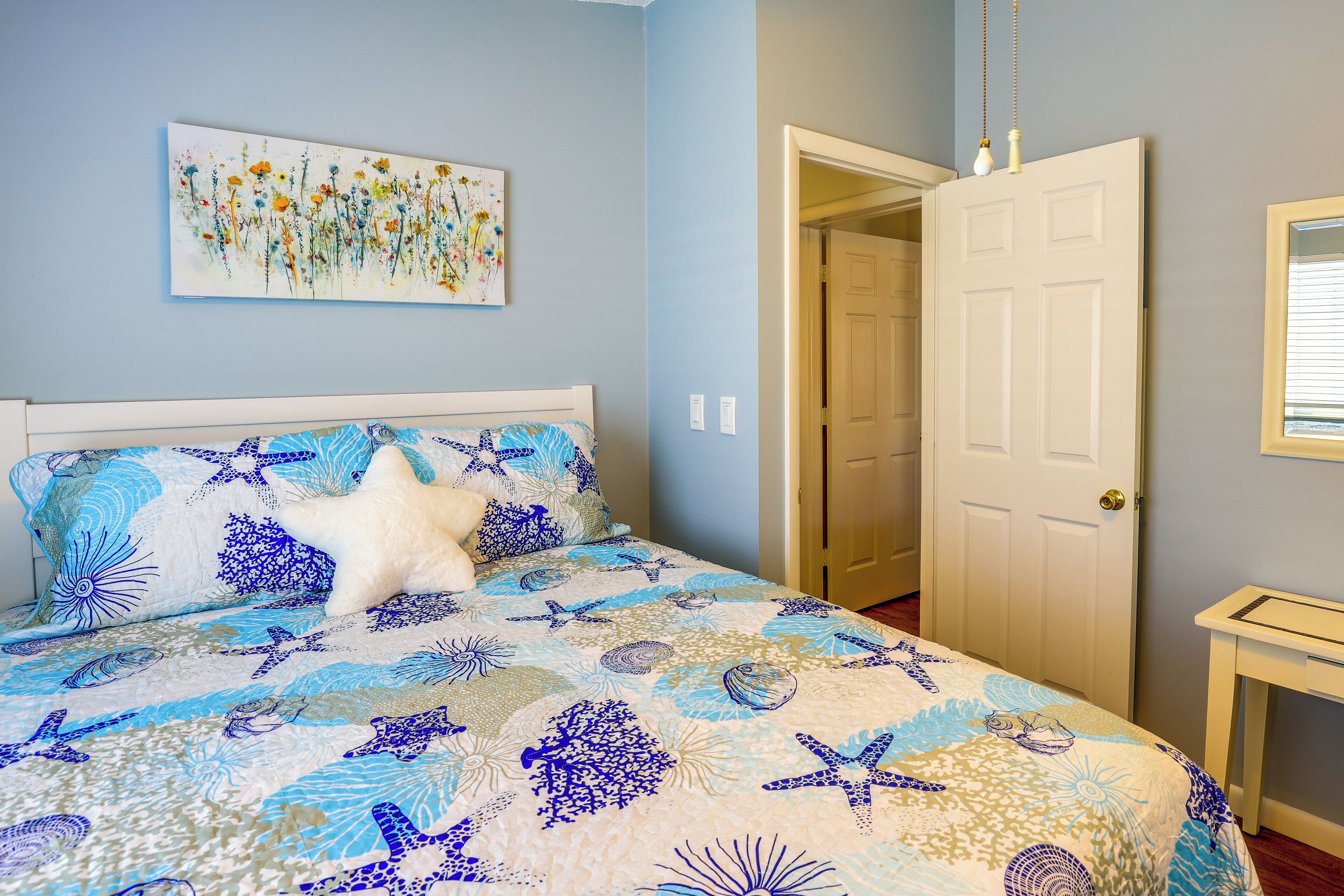 Una camera da letto con un letto caratterizzato da un motivo floreale e stelle marine blu e bianche, un cuscino a forma di stella bianca e un quadro con fiori appeso al muro.