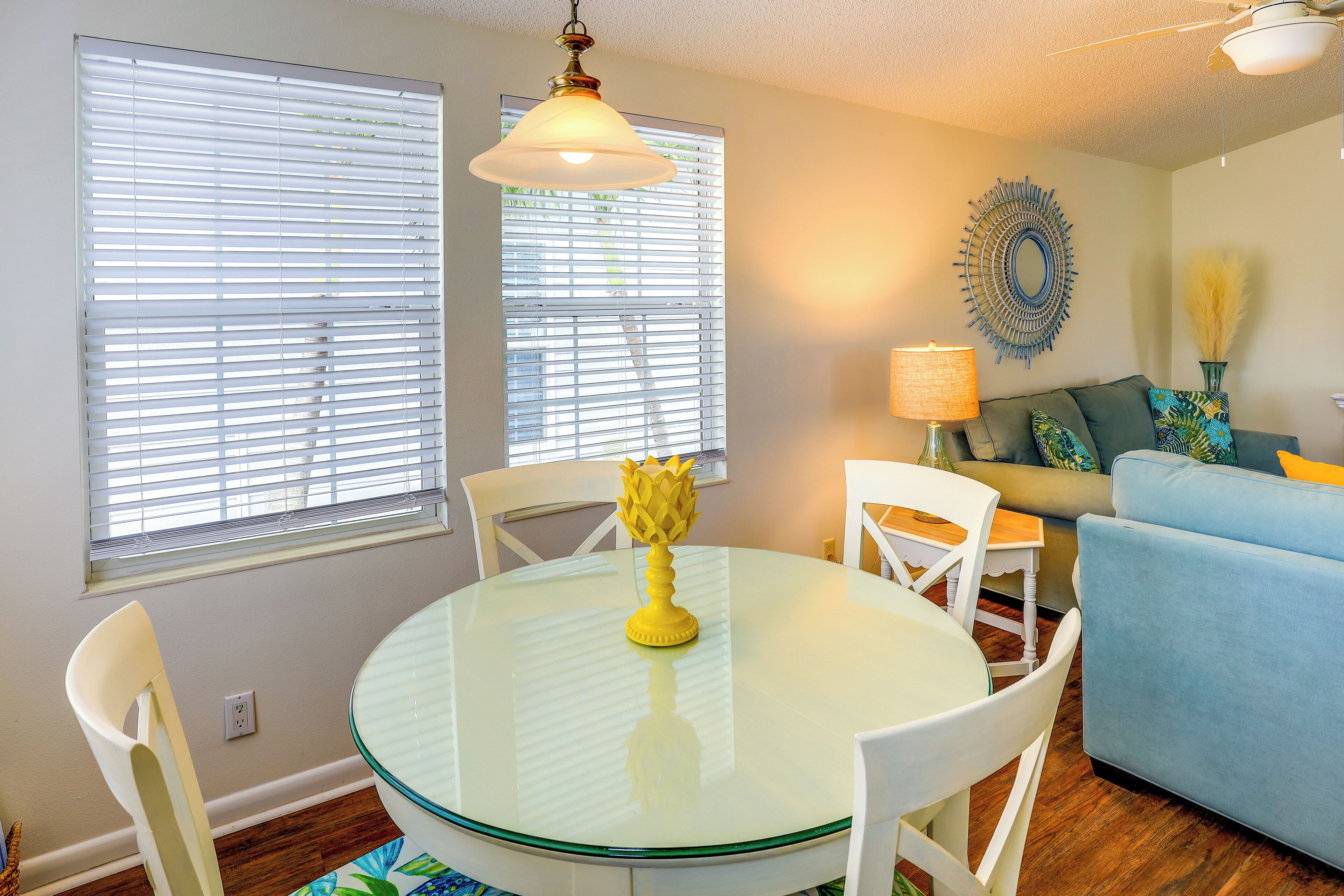A dining area with a glass table, white chairs, and a yellow vase.