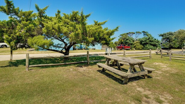 Un tavolo da picnic in una zona erbosa, con un albero e un veicolo rosso sullo sfondo.