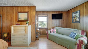 Un'accogliente stanza con pareti in legno, un divano verde, una cassettiera in legno e una finestra con vista.