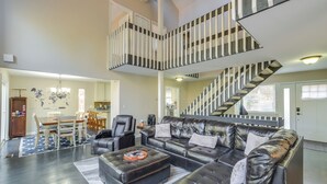 Un salon spacieux avec un grand canapé en cuir noir, une table à manger avec des chaises et un escalier doté d’une rampe à rayures.