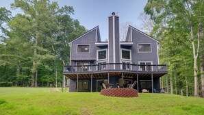 Une maison à deux étages avec un balcon, entourée d’une cour verdoyante et d’arbres.