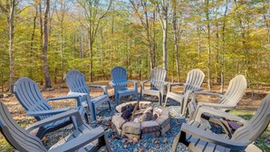 Un espace de détente circulaire aménagé autour d’un foyer, avec des fauteuils Adirondack, situé dans une zone boisée.