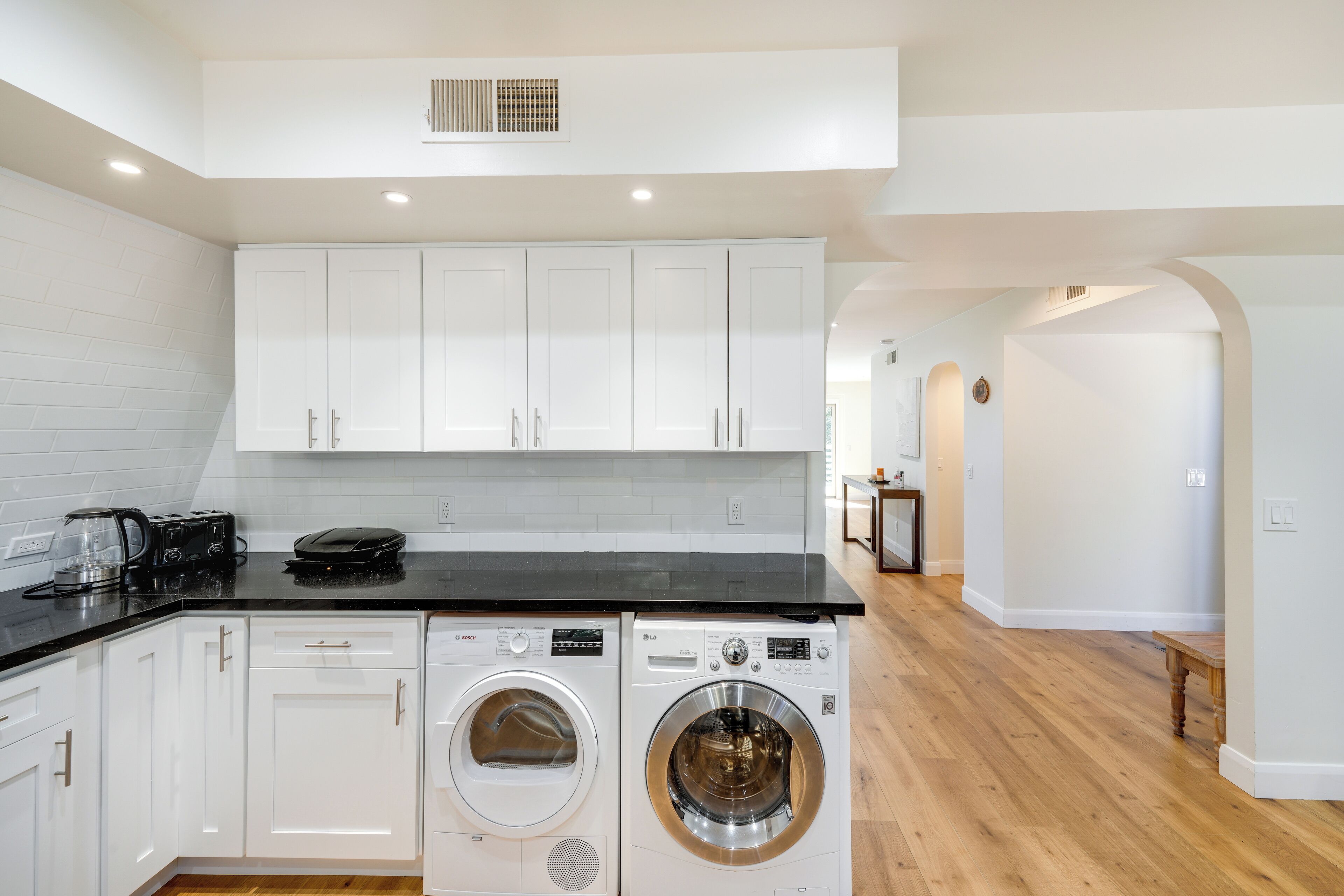 A modern kitchen with white cabinets, a black countertop, and a washing machine.