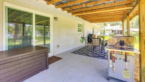 Un patio couvert équipé d’un barbecue, d’un banc en bois et d’un coin repas avec des chaises.