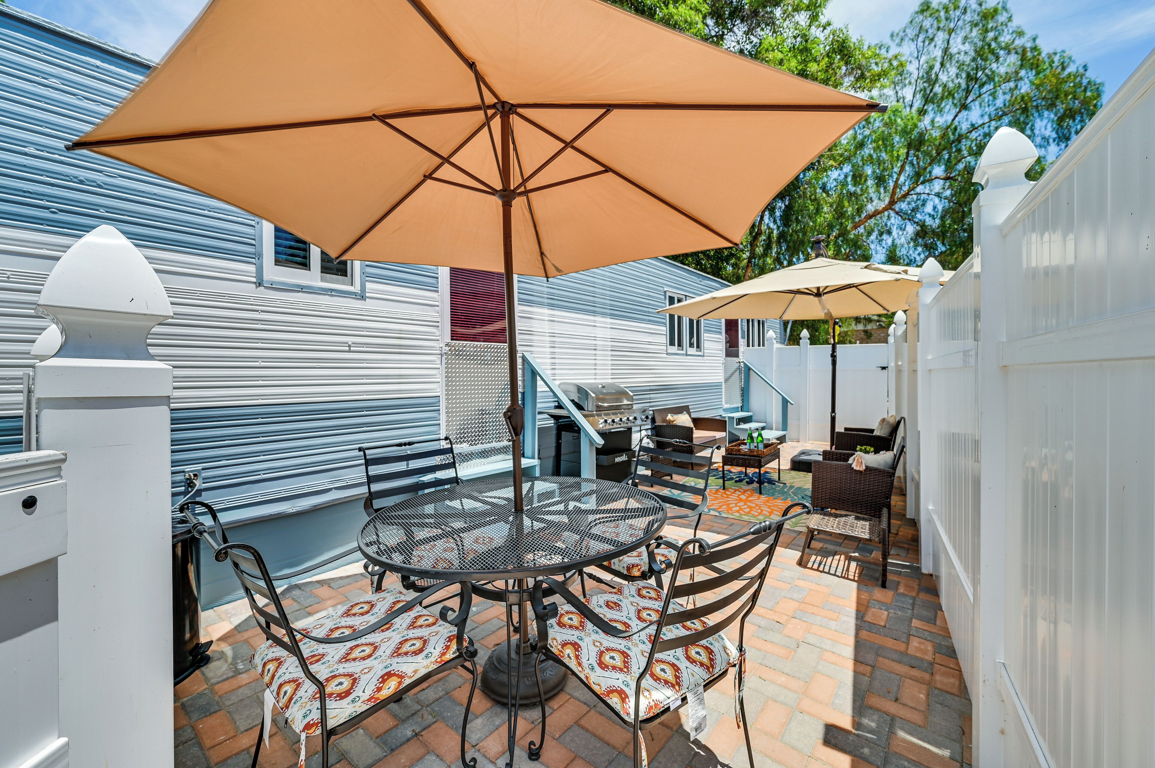Eine Terrasse mit einem runden Metalltisch und Stühlen, einem großen, beigen Sonnenschirm und einem Grill.