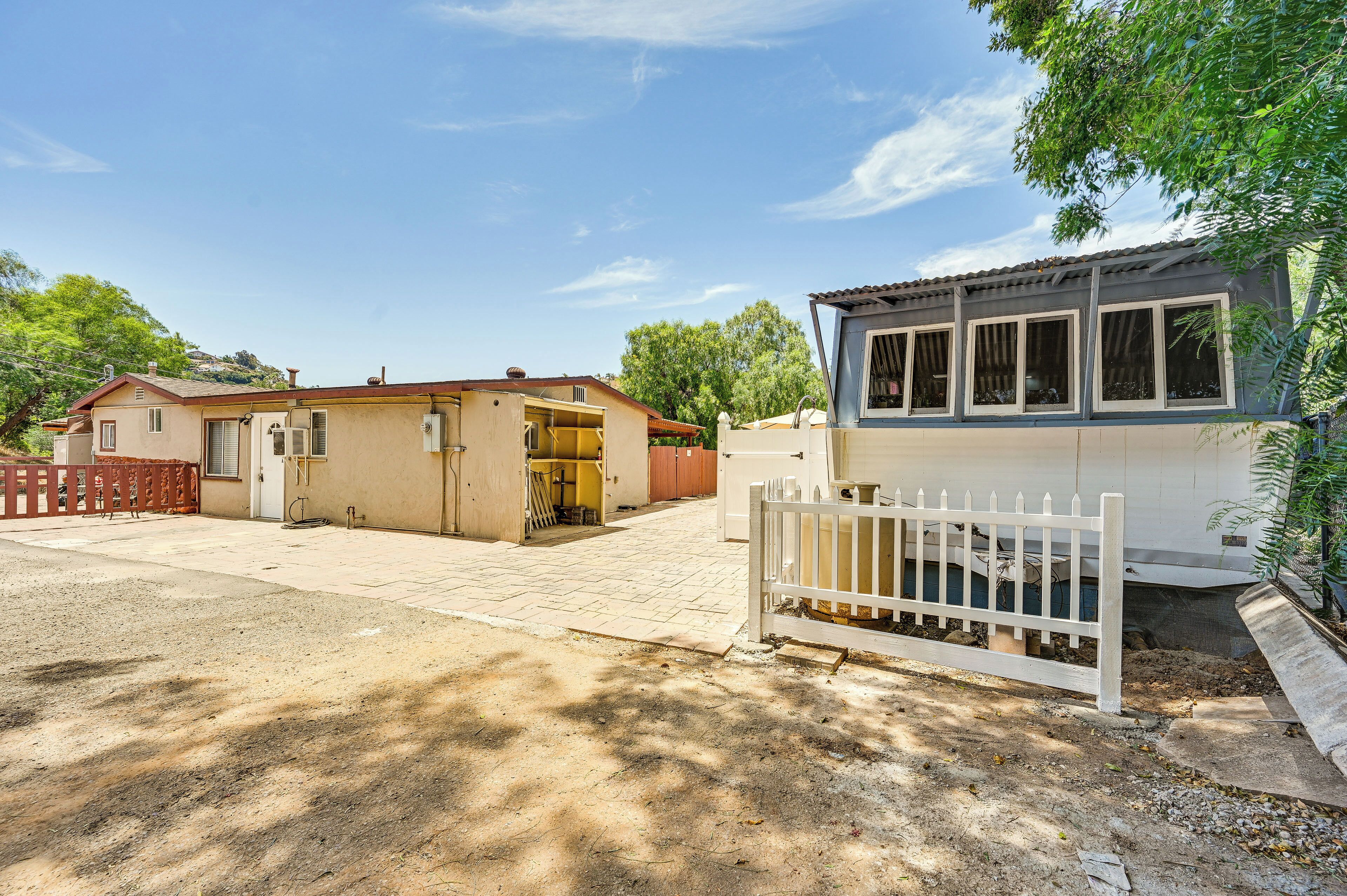 A residential property with a paved driveway, a white picket fence, and a small building with a garage.