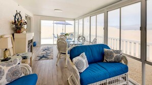 A sunlit room with wicker furniture, a blue sofa, and a view of the beach. - Between the Dunes: Breezy Beachfront Oceano Home! (Oceano)