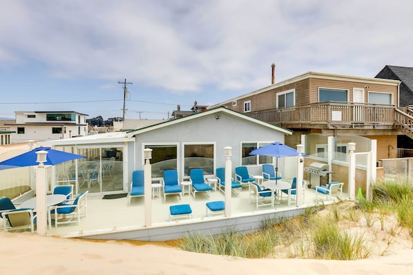 A beach house with a covered patio, outdoor seating, and a view of the ocean.