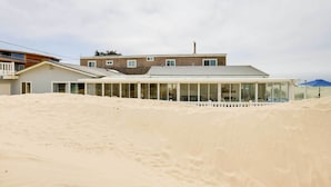 A modern building with a flat roof and large windows, surrounded by sand dunes. - Between the Dunes: Breezy Beachfront Oceano Home! (Oceano)
