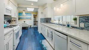 A modern kitchen with white cabinets, a blue backsplash, and a view of the beach through a window. - Between the Dunes: Breezy Beachfront Oceano Home! (Oceano)