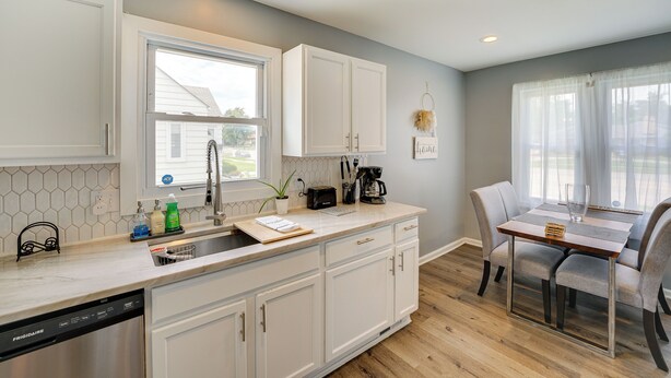 A modern kitchen with white cabinets, a dishwasher, and a dining area with a table and chairs. - Pet-friendly Southfield House w/ Ping-pong Table! (Southfield)