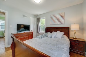 A bedroom with a wooden bed, a television, a nightstand with a lamp, and a painting on the wall.