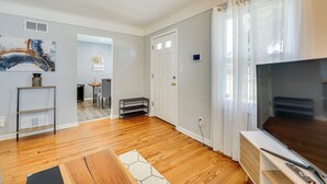 A living room with hardwood flooring, a TV, a sofa, and a coffee table. There is a door leading to another room and a small table with chairs. - Pet-friendly Southfield House w/ Ping-pong Table! (Southfield)