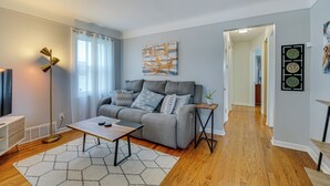 A modern living room with a grey sofa, a coffee table, and a floor lamp. There is a painting on the wall and a plant on a side table. - Pet-friendly Southfield House w/ Ping-pong Table! (Southfield)