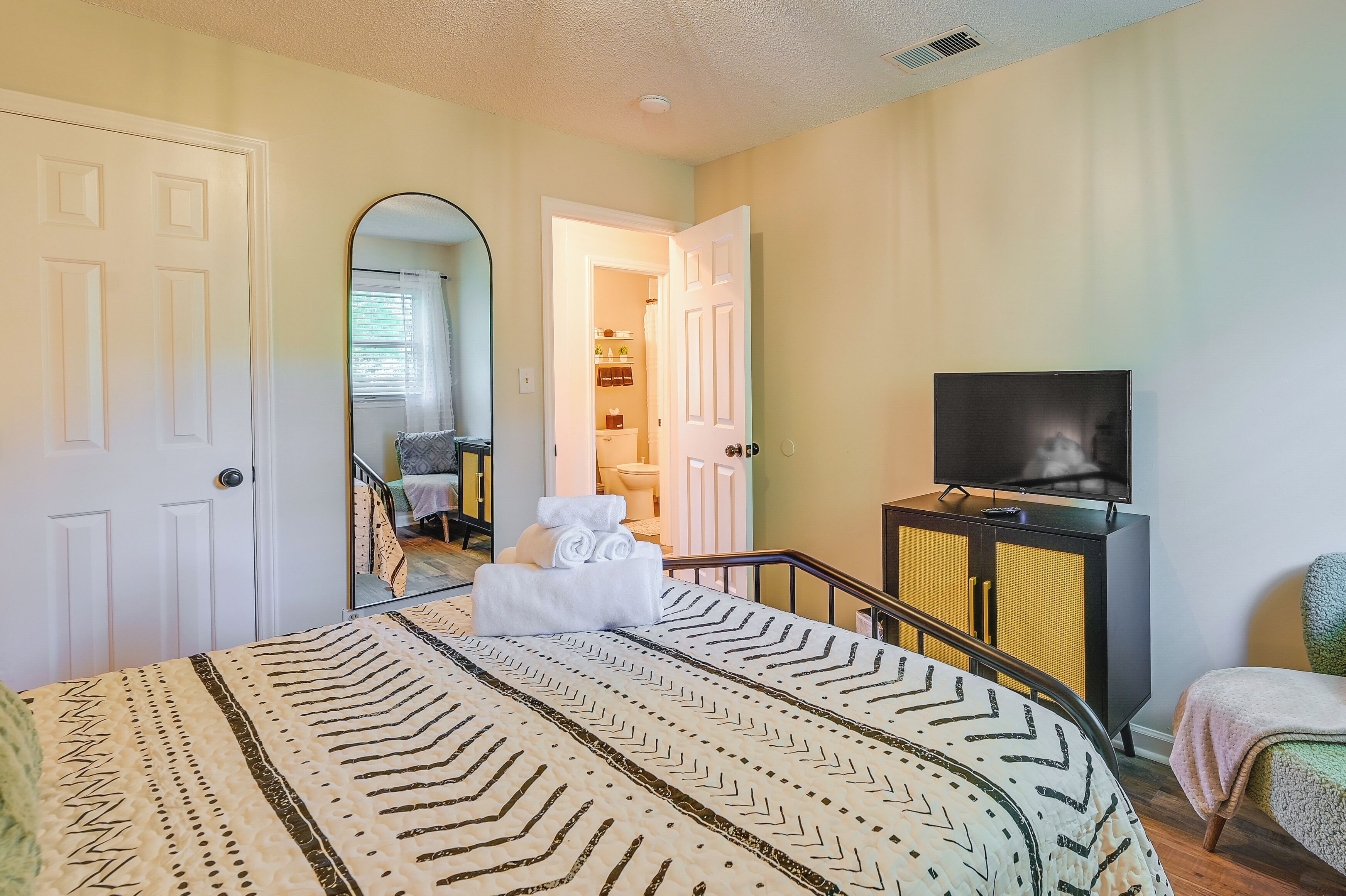 A bedroom with a bed, a TV, a bathroom visible through an open door, and a staircase.