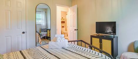 A bedroom with a bed, a TV, a bathroom visible through an open door, and a staircase.