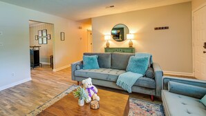 A living room with a grey sofa, a wooden coffee table, and a teddy bear. There is a mirror on the wall and a door in the background. - Cozy High Point Vacation Rental: Near HPU Campus (High Point)