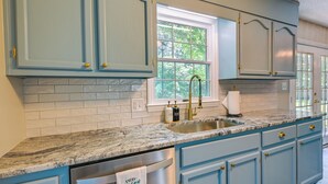 A kitchen with light blue cabinets, a granite countertop, a stainless steel dishwasher, and a window with a view of trees. - Cozy High Point Vacation Rental: Near HPU Campus (High Point)