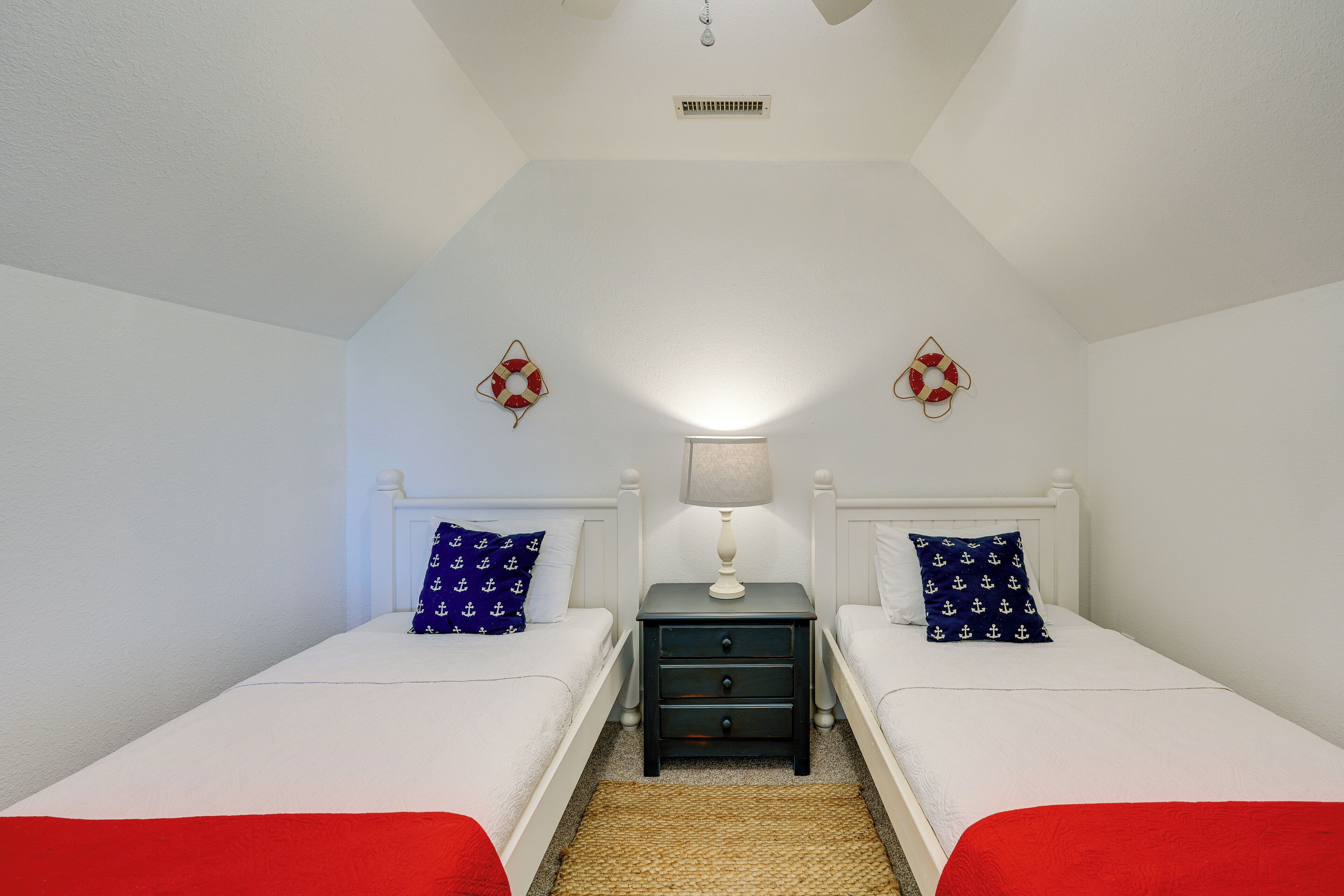 A bedroom with two beds, a nightstand with a lamp, and a ceiling fan.