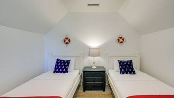 A bedroom with two beds, a nightstand with a lamp, and a ceiling fan.