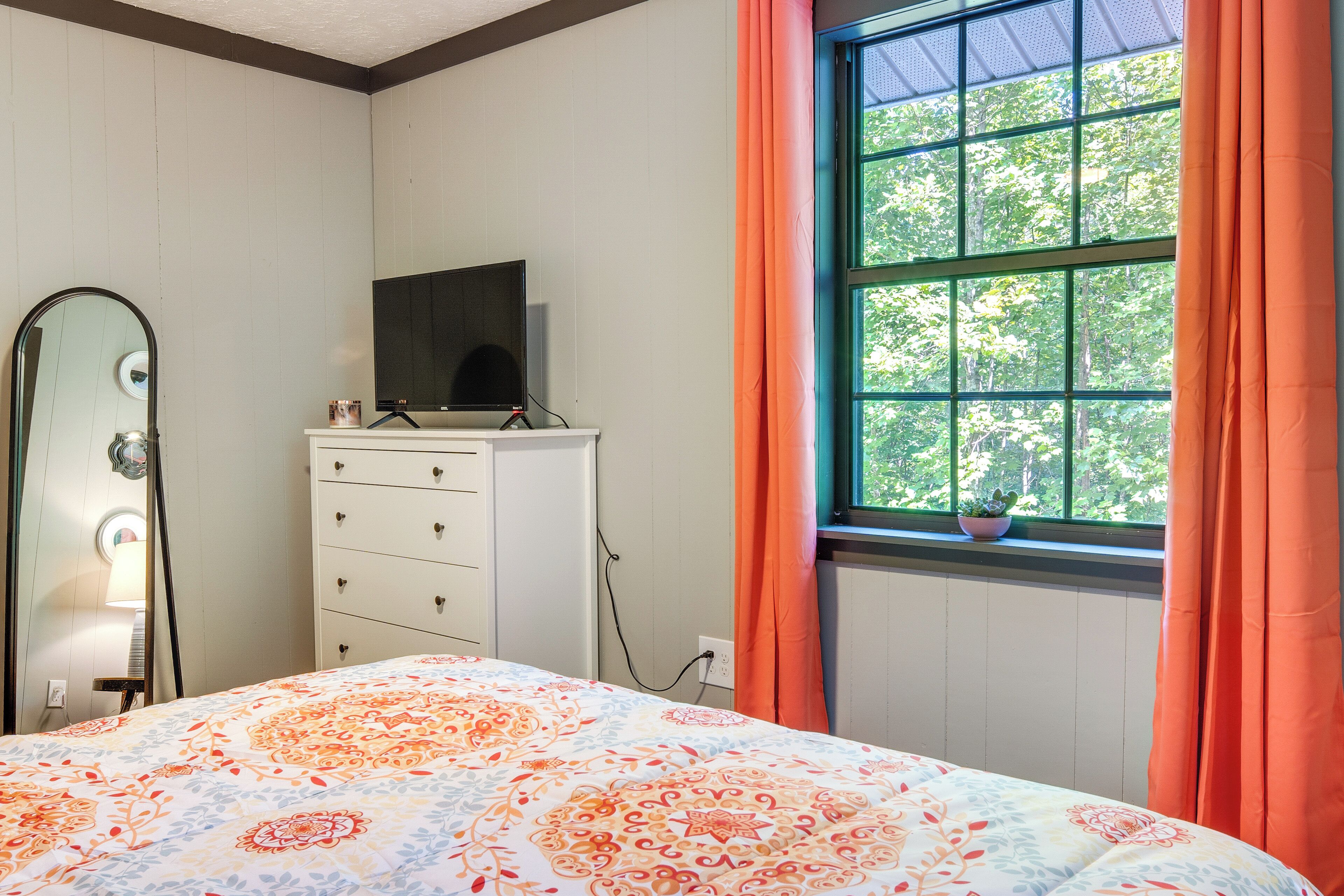 A bedroom with a bed, dresser, TV, and window with curtains.
