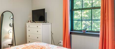 A bedroom with a bed, dresser, TV, and window with curtains.