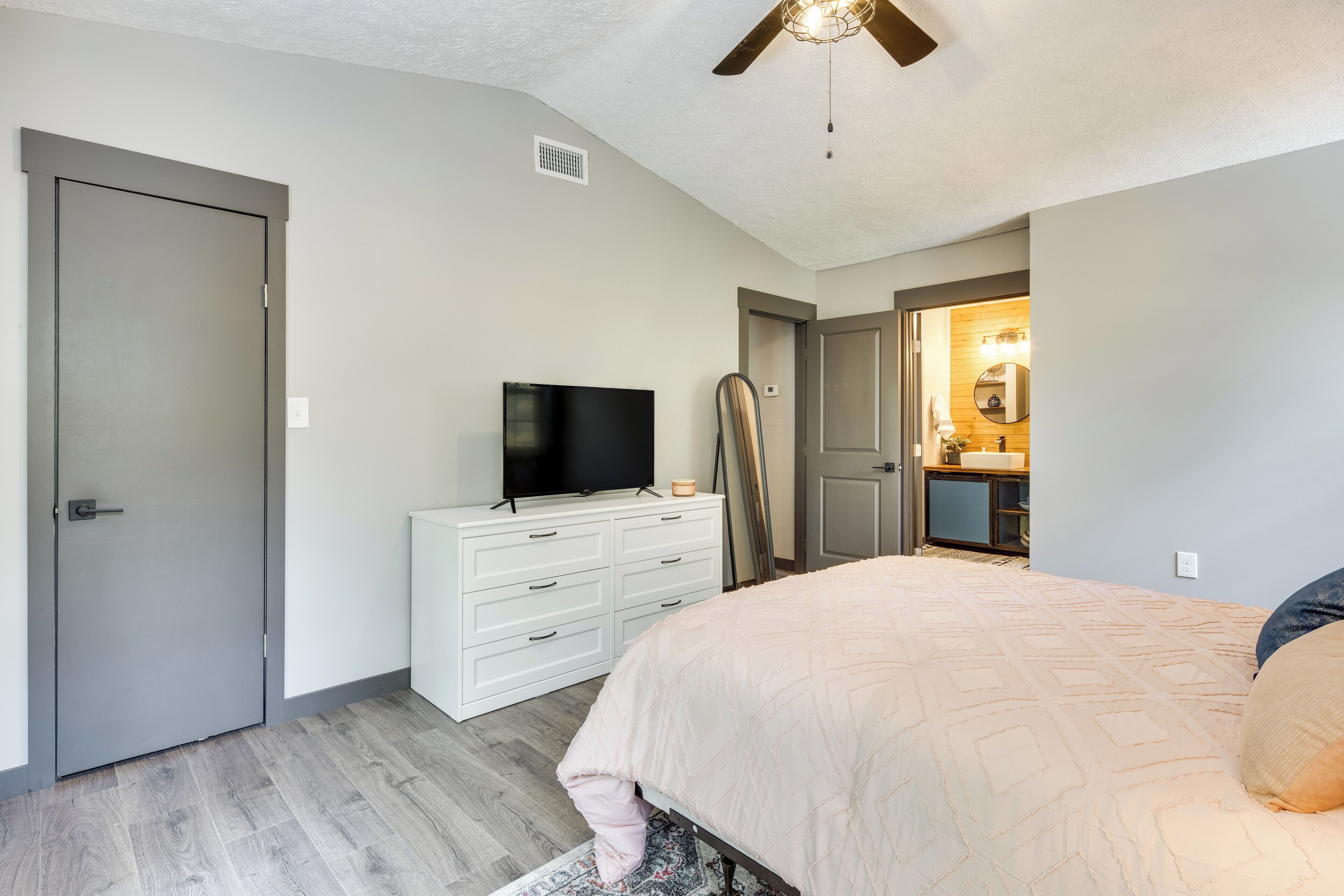 A bedroom with a bed, a dresser, a television, and a ceiling fan.