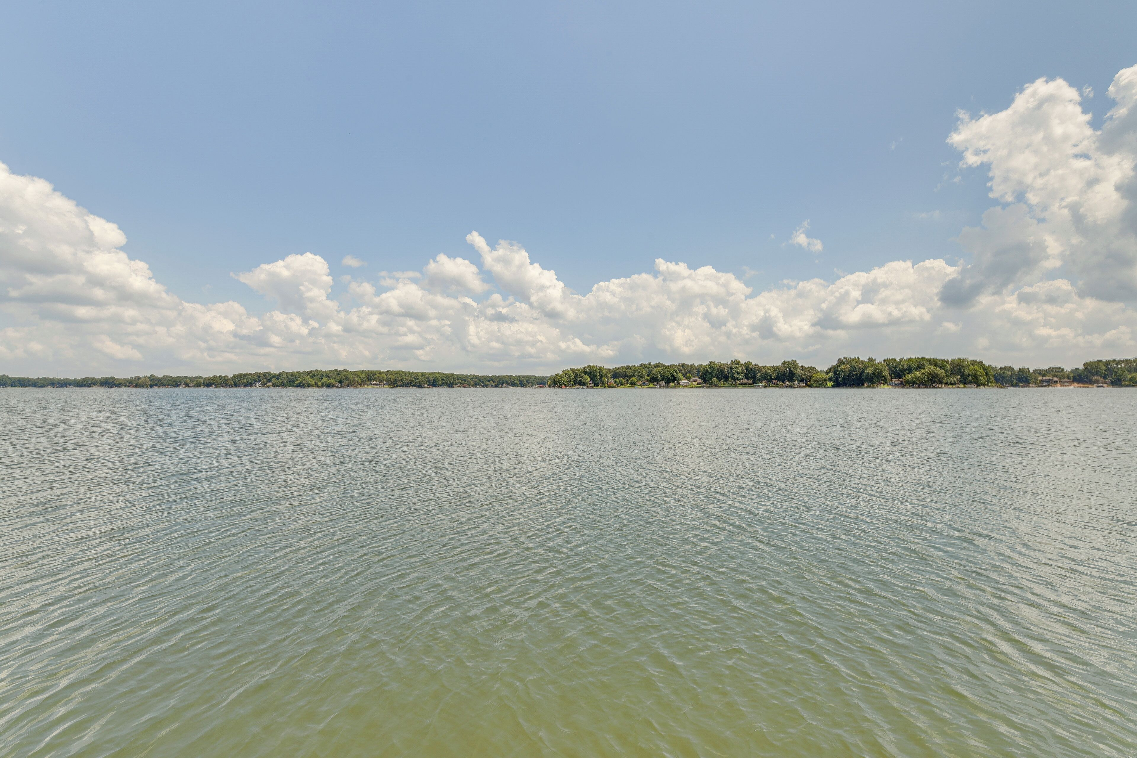 Un lago tranquilo con una orilla lejana de árboles y edificios.