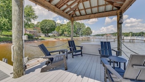 Une terrasse en bois couverte, dotée de sièges et offrant une vue sur un plan d’eau.