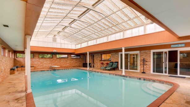 Une piscine intérieure dotée d’un toit en verre, de murs en briques et d’un espace détente agrémenté d’une enseigne indiquant « Salon au bord de la piscine ».