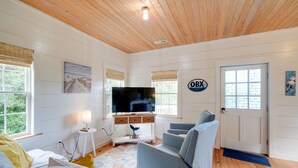 A cozy living room with a wooden ceiling, a flat-screen TV on a white stand, and a door with a window. - Charming Buxton Vacation Rental Near Beaches (Buxton)