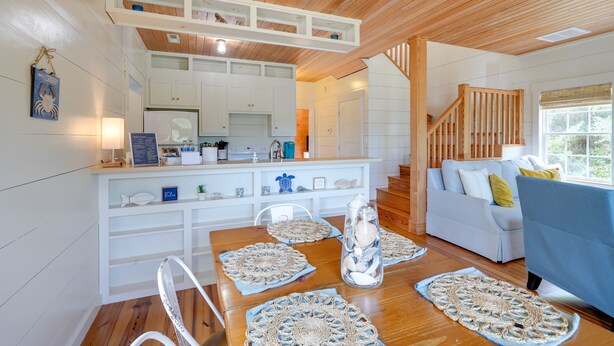 A cozy living room with a wooden ceiling, a white sofa, a blue armchair, and a dining table with crocheted placemats. - Charming Buxton Vacation Rental Near Beaches (Buxton)