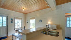 A kitchen with a wooden ceiling, a large island with a sink, and a window with blinds. - Charming Buxton Vacation Rental Near Beaches (Buxton)