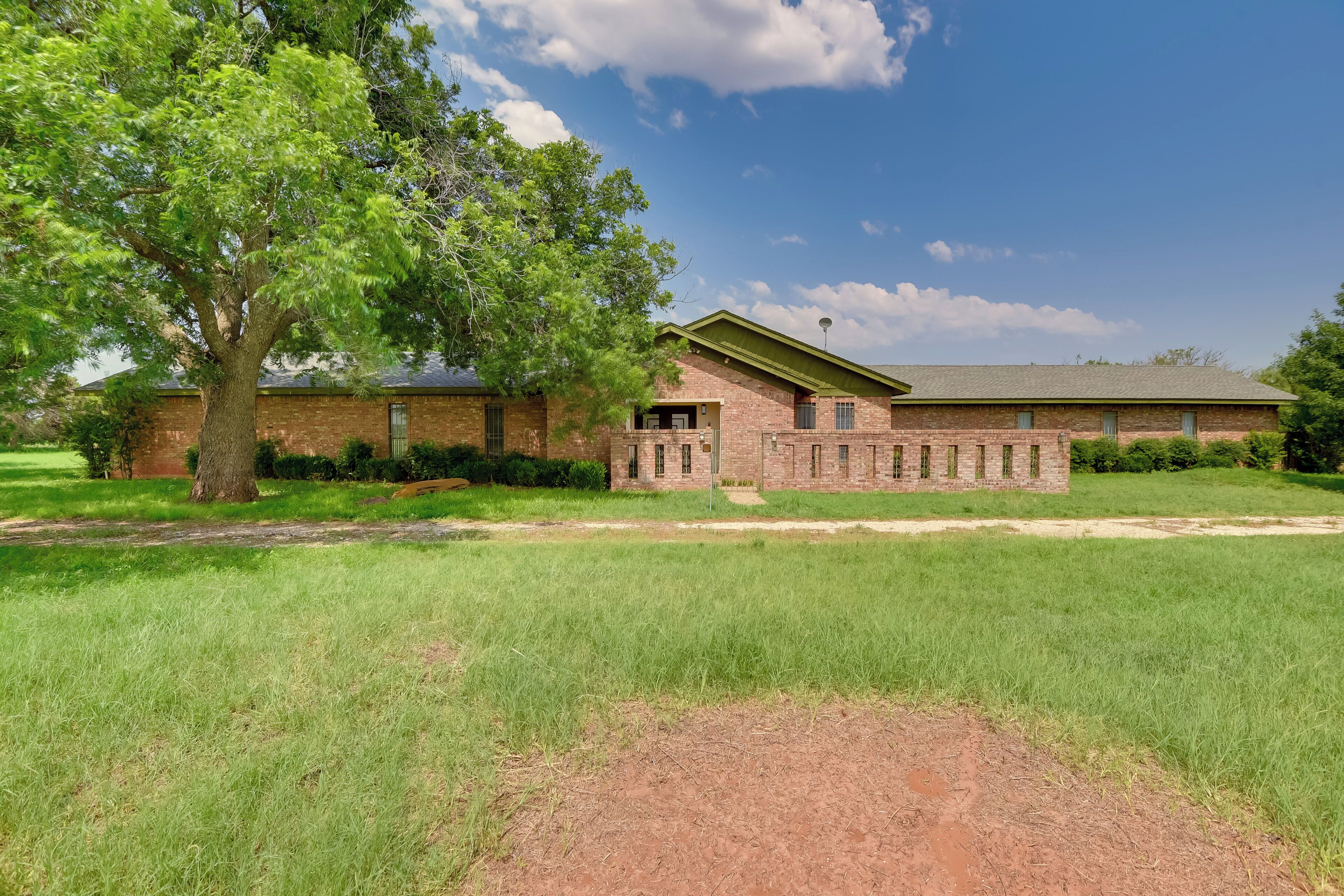 A brick building with a green roof, surrounded by a well-maintained lawn and a large tree.