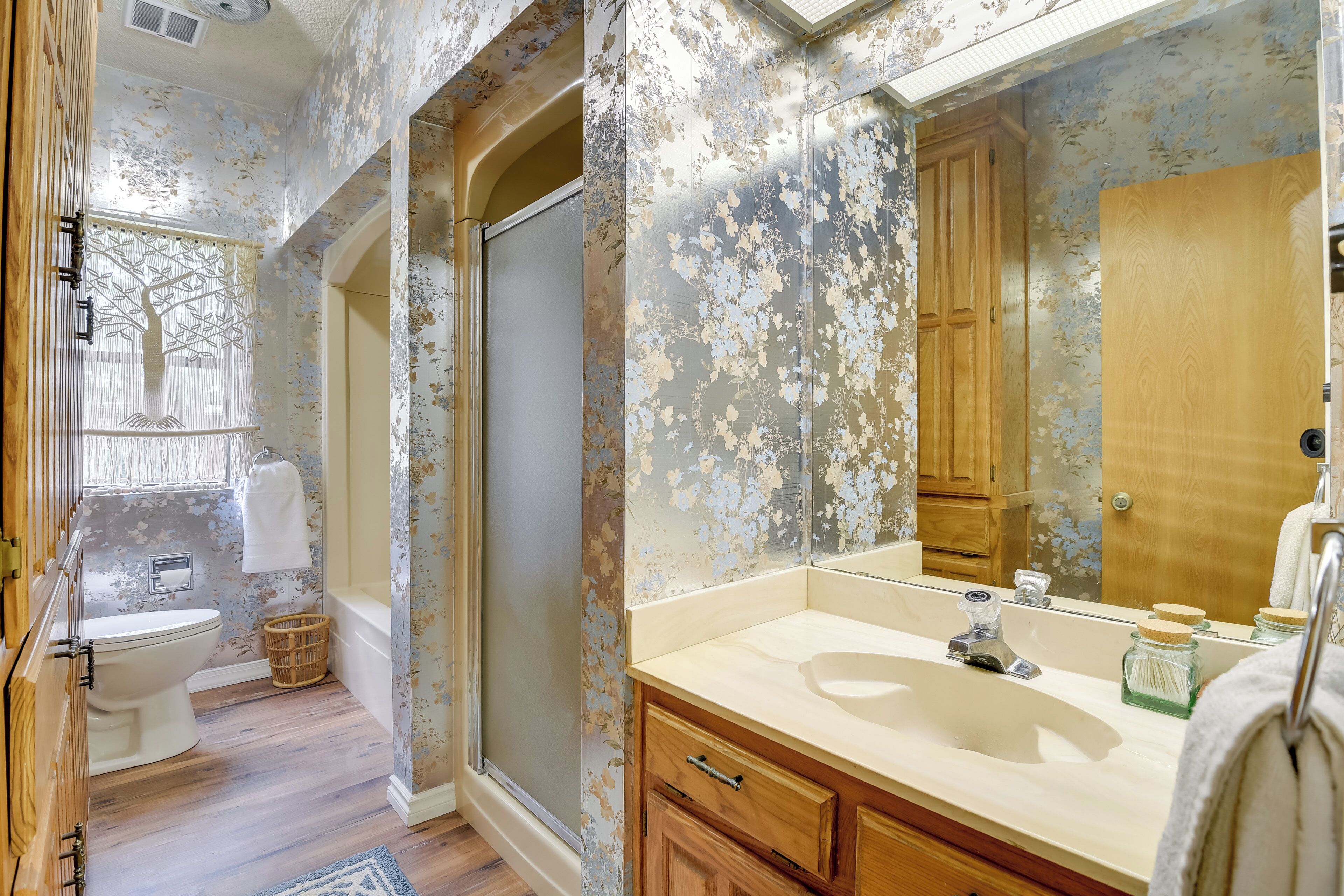 A bathroom with a large mirror, wooden cabinets, a white sink, and a shower area.