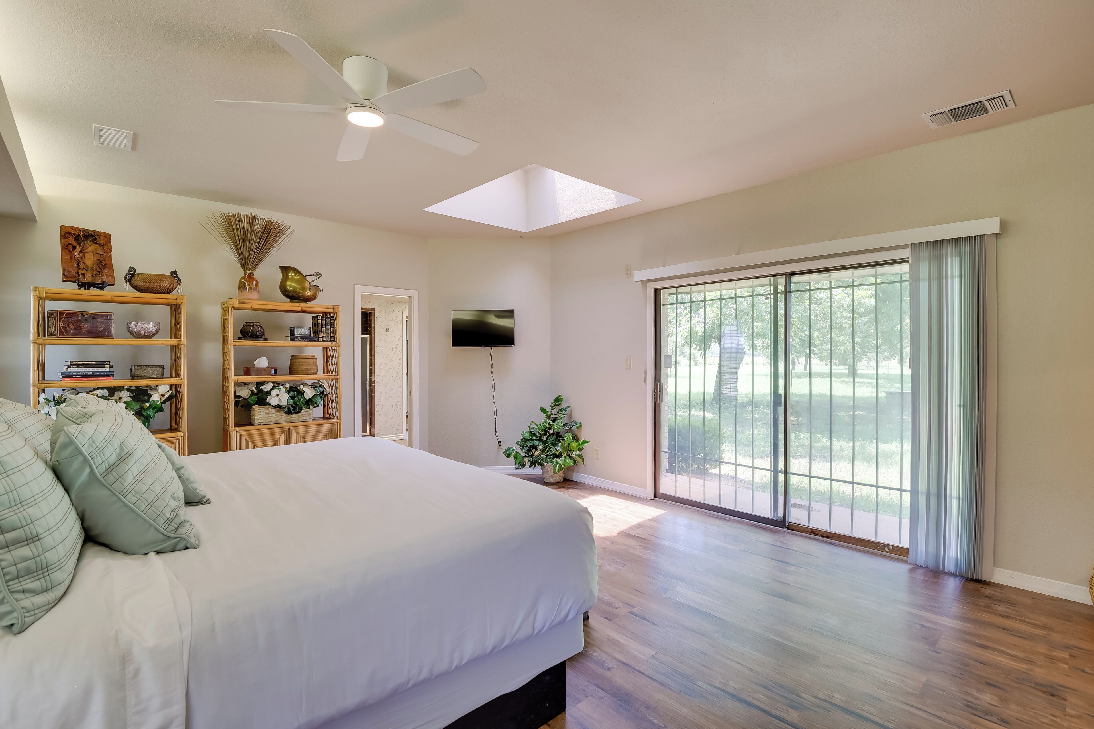 Une chambre spacieuse avec un grand lit, un ventilateur de plafond, une télévision et une porte-fenêtre coulissante donnant sur un balcon.