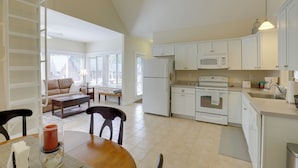 Una cocina amplia con armarios blancos, microondas, horno y refrigerador. Hay un comedor con mesa y sillas, y una sala de estar con sofá y mesa de centro.