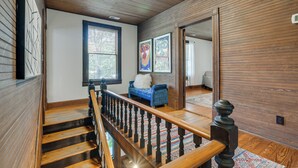 Eine Holztreppe mit Handlauf führt zu einem Raum mit einem blauen Sofa und einem Fenster mit Jalousien.