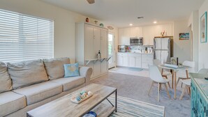 A modern living room with a sofa, coffee table, and a ceiling fan. A kitchen with white cabinets and a dining area with chairs is visible in the background. - Newly Built Sparks Home w/ Hot Tub: 12 Mi to Reno! (Sparks)