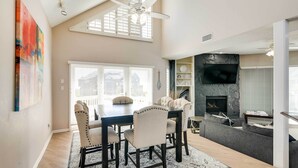 A dining area with a dark wooden table and beige upholstered chairs, a fireplace, and a stone accent wall.