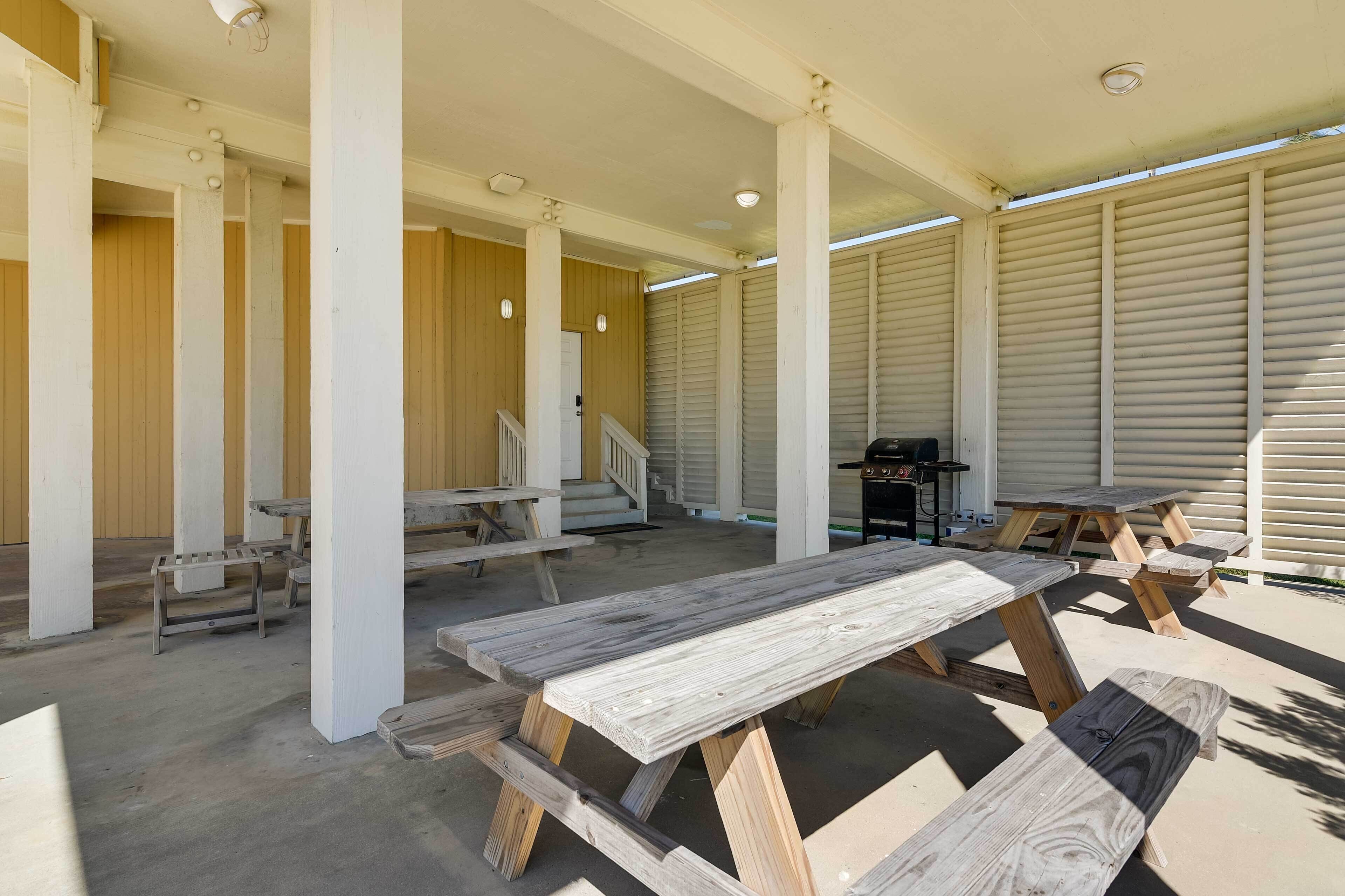 Un espace extérieur aménagé en terrasse, avec des tables et des bancs en bois, un barbecue et une allée couverte soutenue par des colonnes.