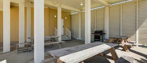 Un espace extérieur aménagé en terrasse, avec des tables et des bancs en bois, un barbecue et une allée couverte soutenue par des colonnes.