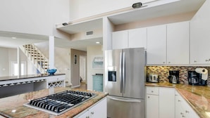 A modern kitchen with white cabinets, a stainless steel refrigerator, a granite countertop, and a built-in gas stove.